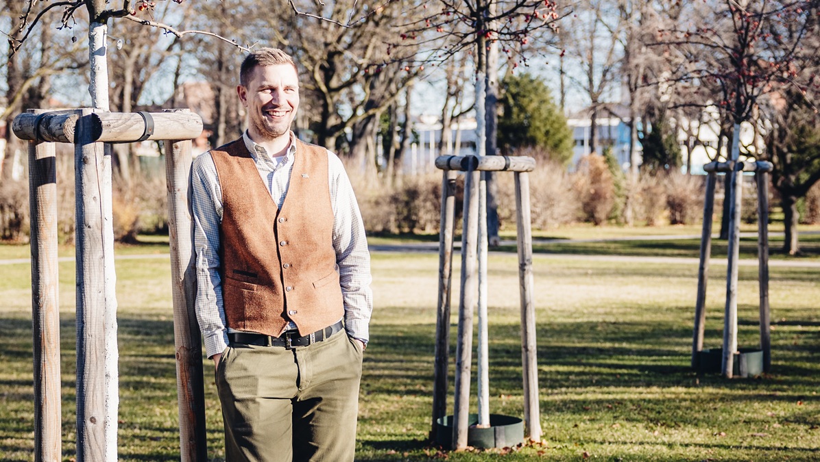 Lächelnder Vater steht in einem Park neben einem jungen Baum