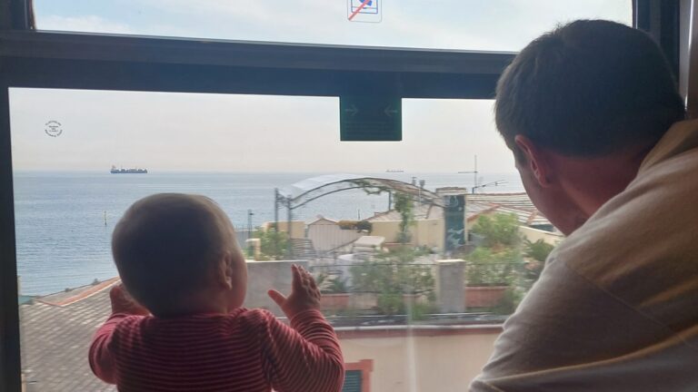 Vater und Kind schauen bei einer Nachtzugreise nach Italien aus dem Zugfenster aufs Meer