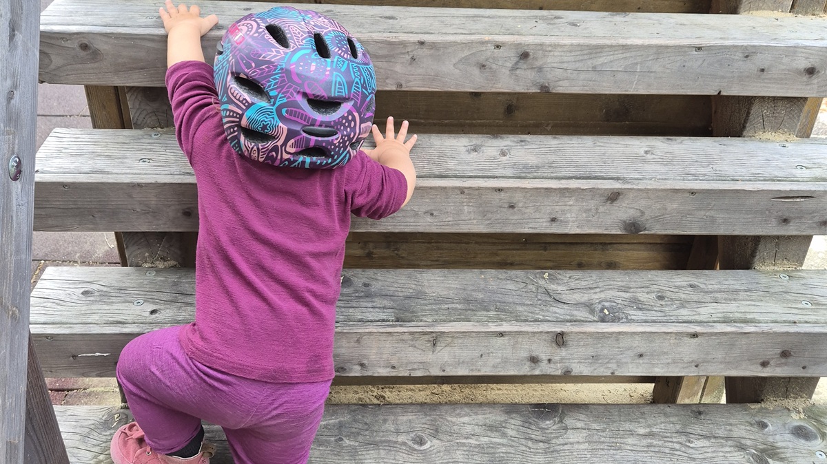 Kind mit Fahrradhelm klettert auf einem Holzspielgerät