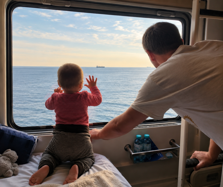Papa und Kleinkind schauen während einer Zugreise gemeinsam aus dem Fenster aufs Meer